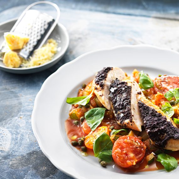 Kycklingfilé toppad med oliv på en bädd av tomat, zucchini & kapris